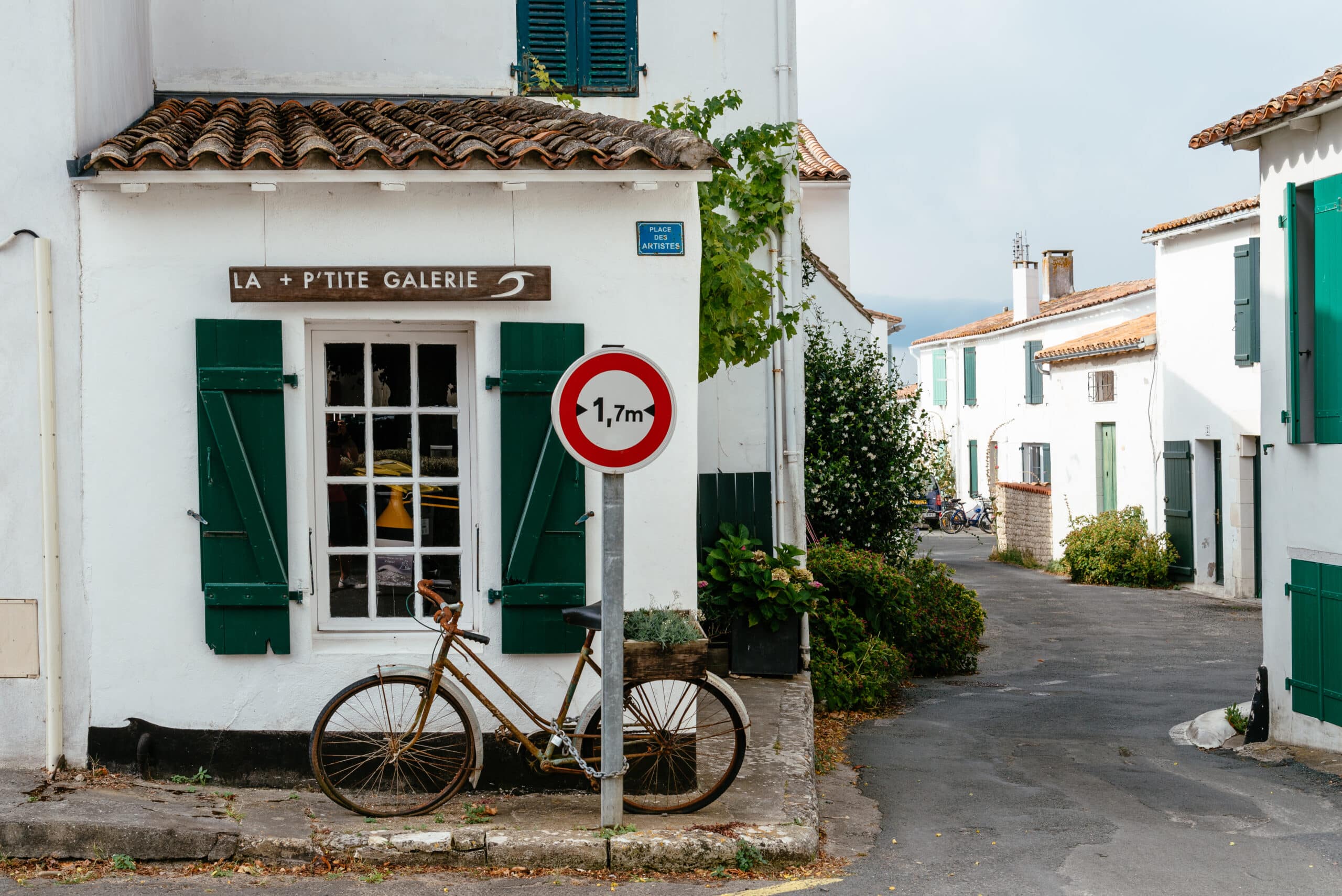 White house with a bicycle, a sign, and green shutters.